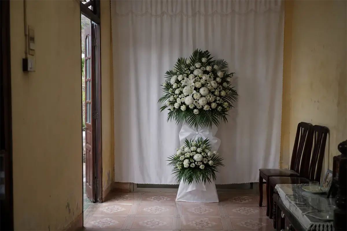 Một kệ hoa viếng tông trắng dáng gọn đặt trong phòng khách hẹp tại tư gia, còn chừa lối đi hai bên